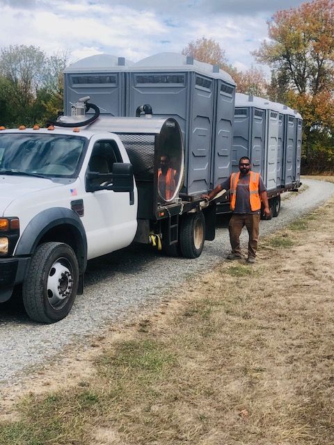 A man is standing next to a truck with portable toilets on the back.