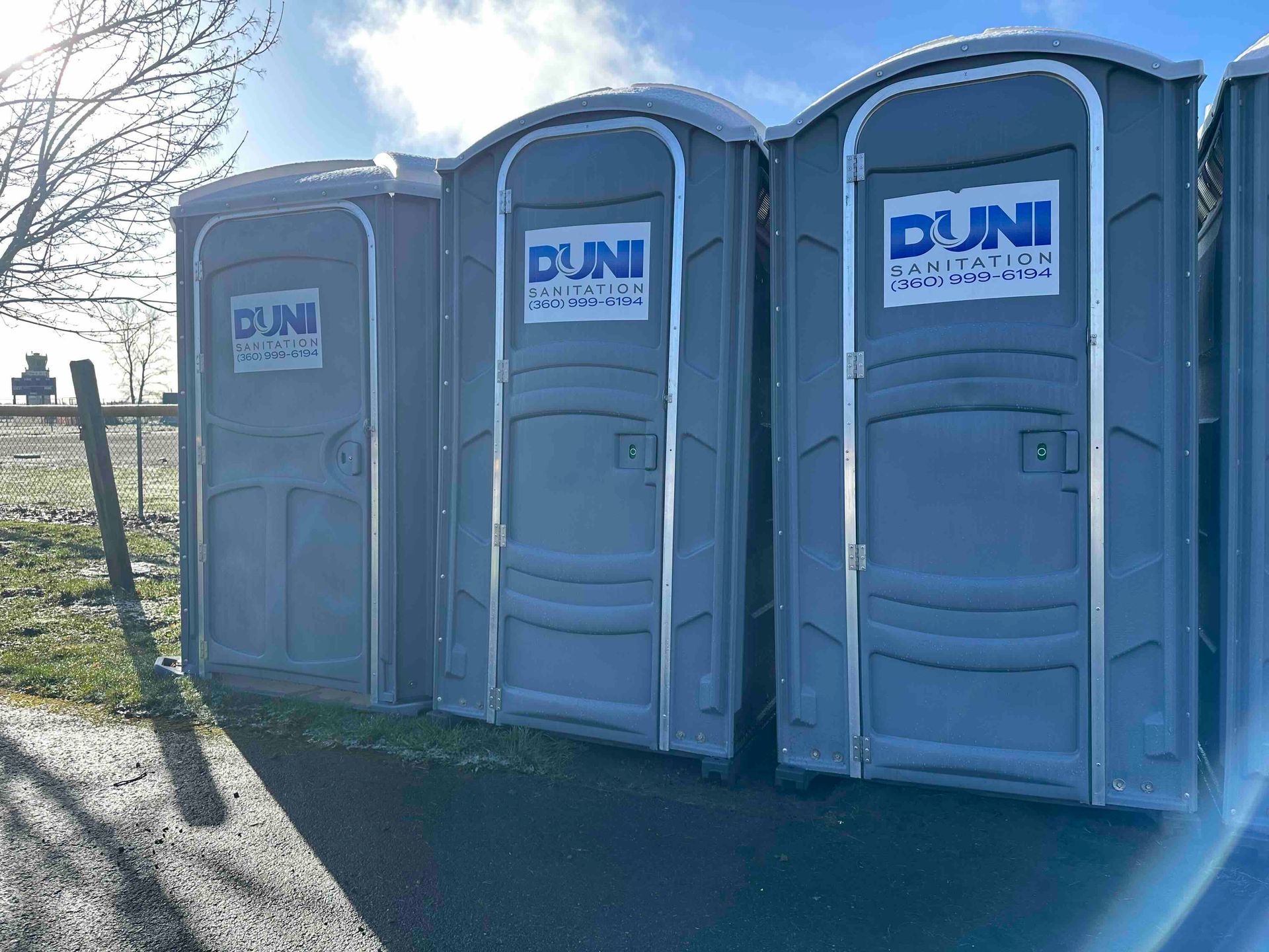 Three portable toilets are lined up next to each other in a parking lot.