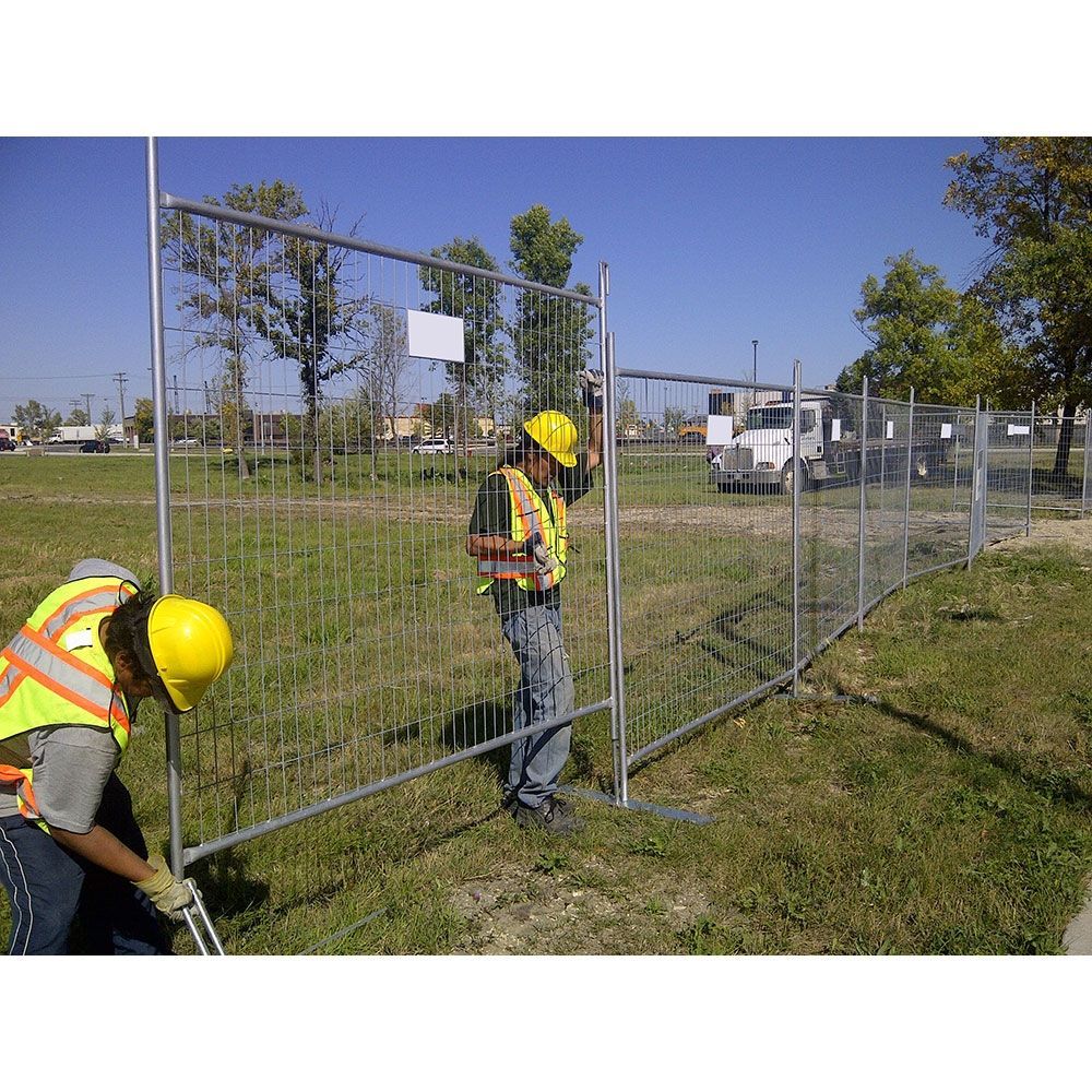 Two construction workers are working on a fence in a field