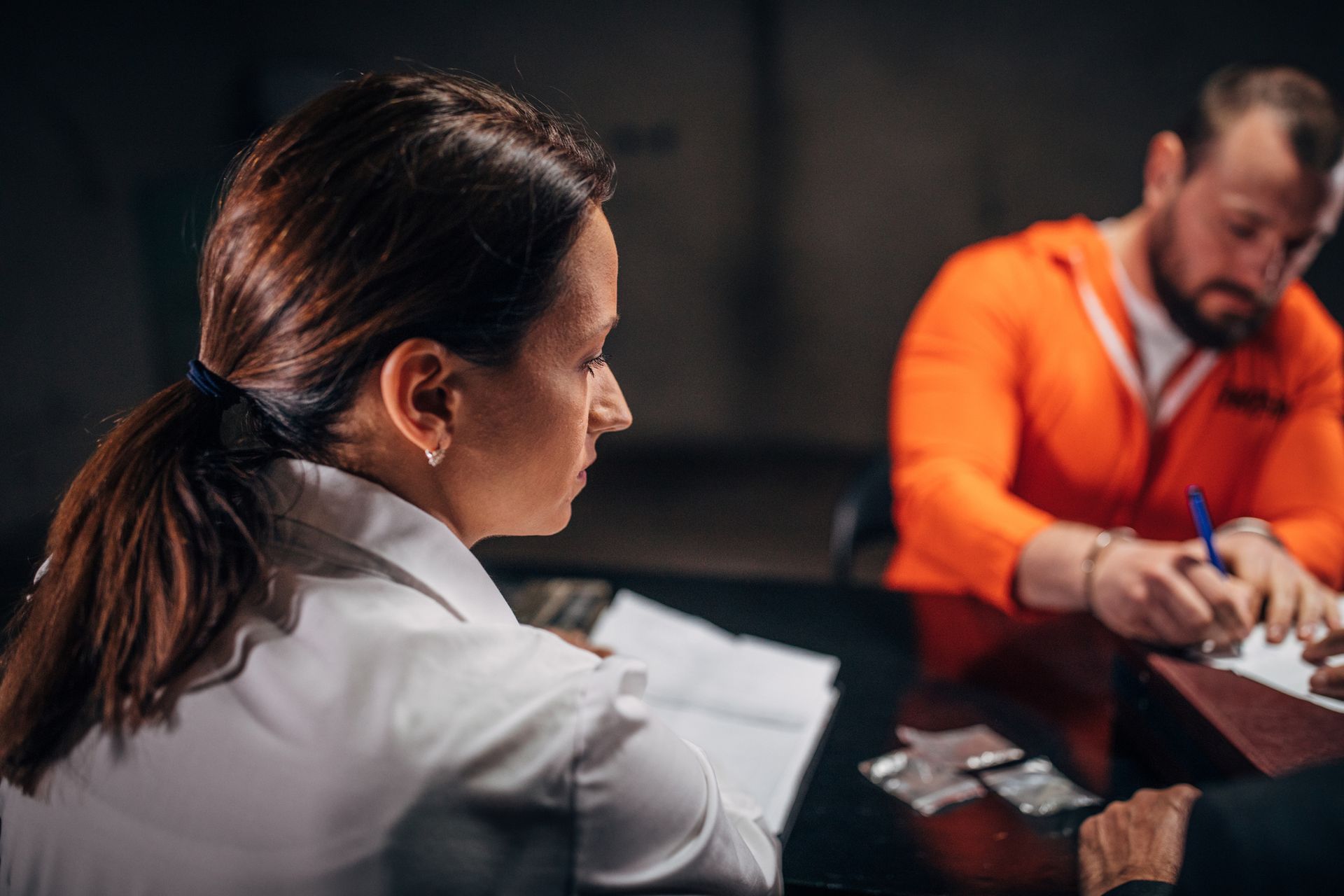 A woman is sitting at a table with a man in an orange jumpsuit.