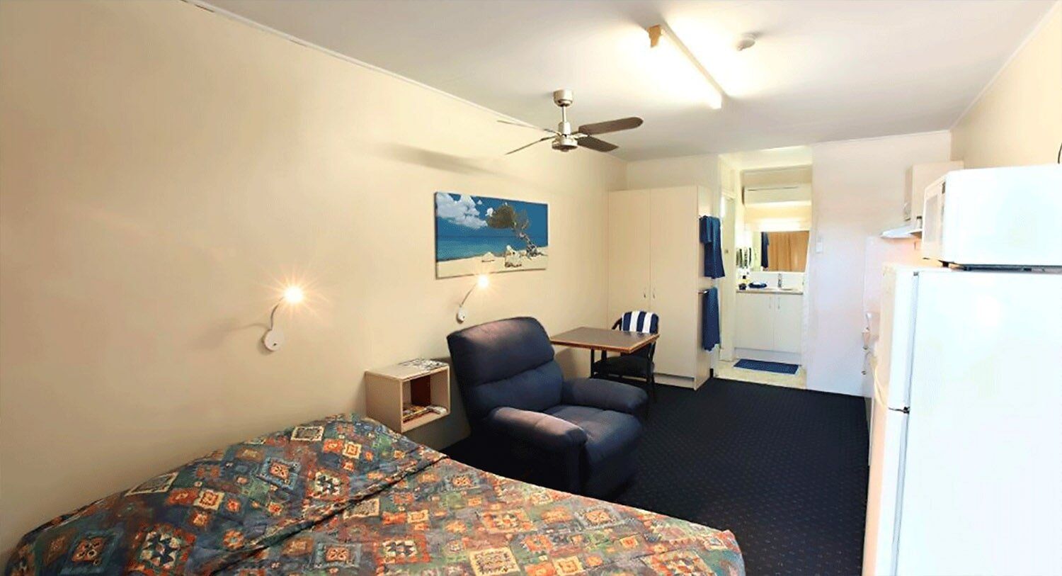 Small motel room: bed, recliner, table, microwave, bathroom. Blue and white color scheme.
