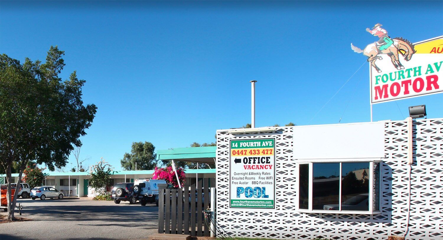 Fourth Avenue Motor Lodge with a sign and a pool under a blue sky.