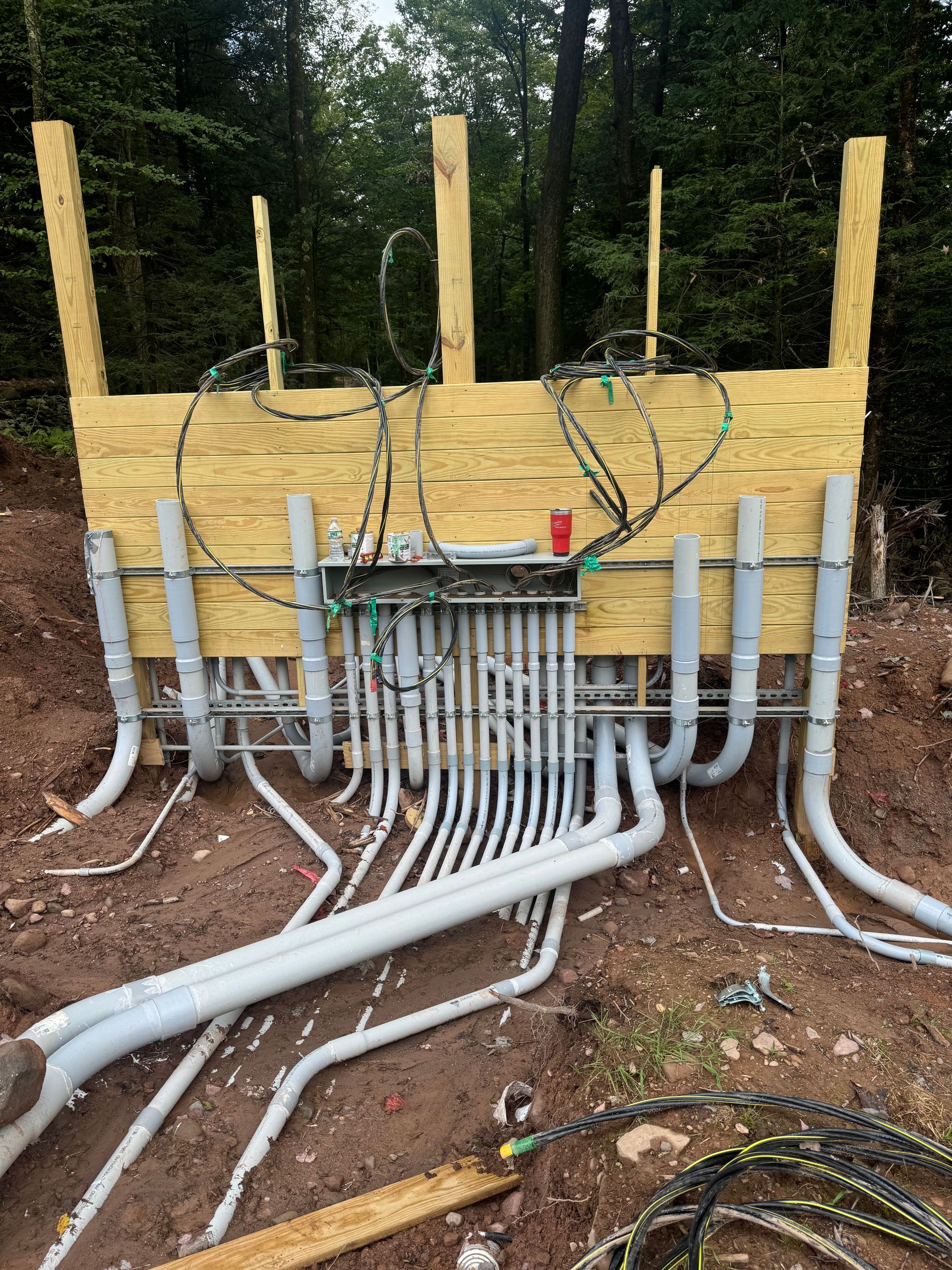 American Electric LLC | A bunch of pipes are sitting on the ground in front of a wooden wall.