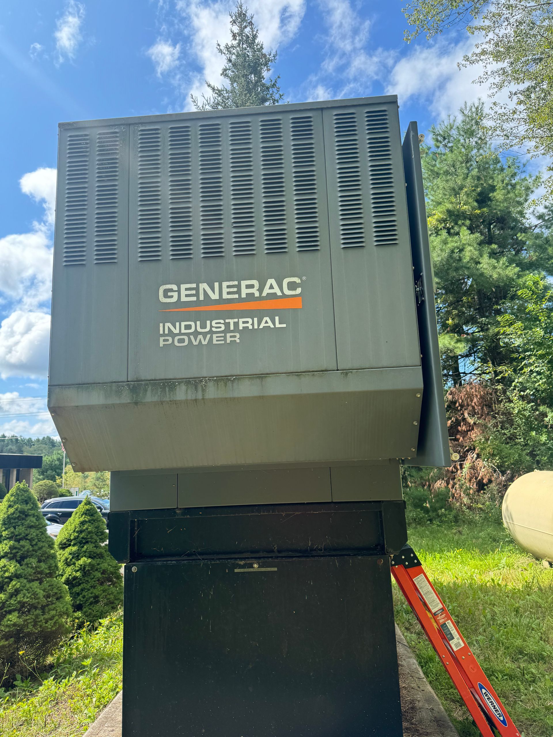American Electric LLC | A generator is sitting in the grass next to a ladder.