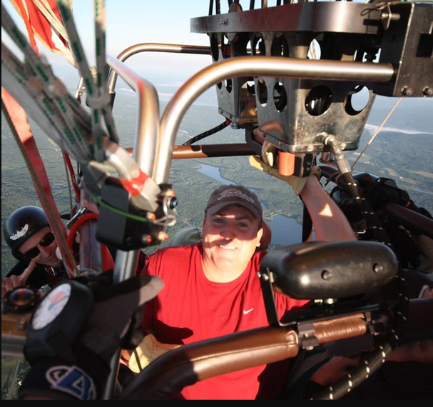 A man in a red shirt is sitting in a hot air balloon