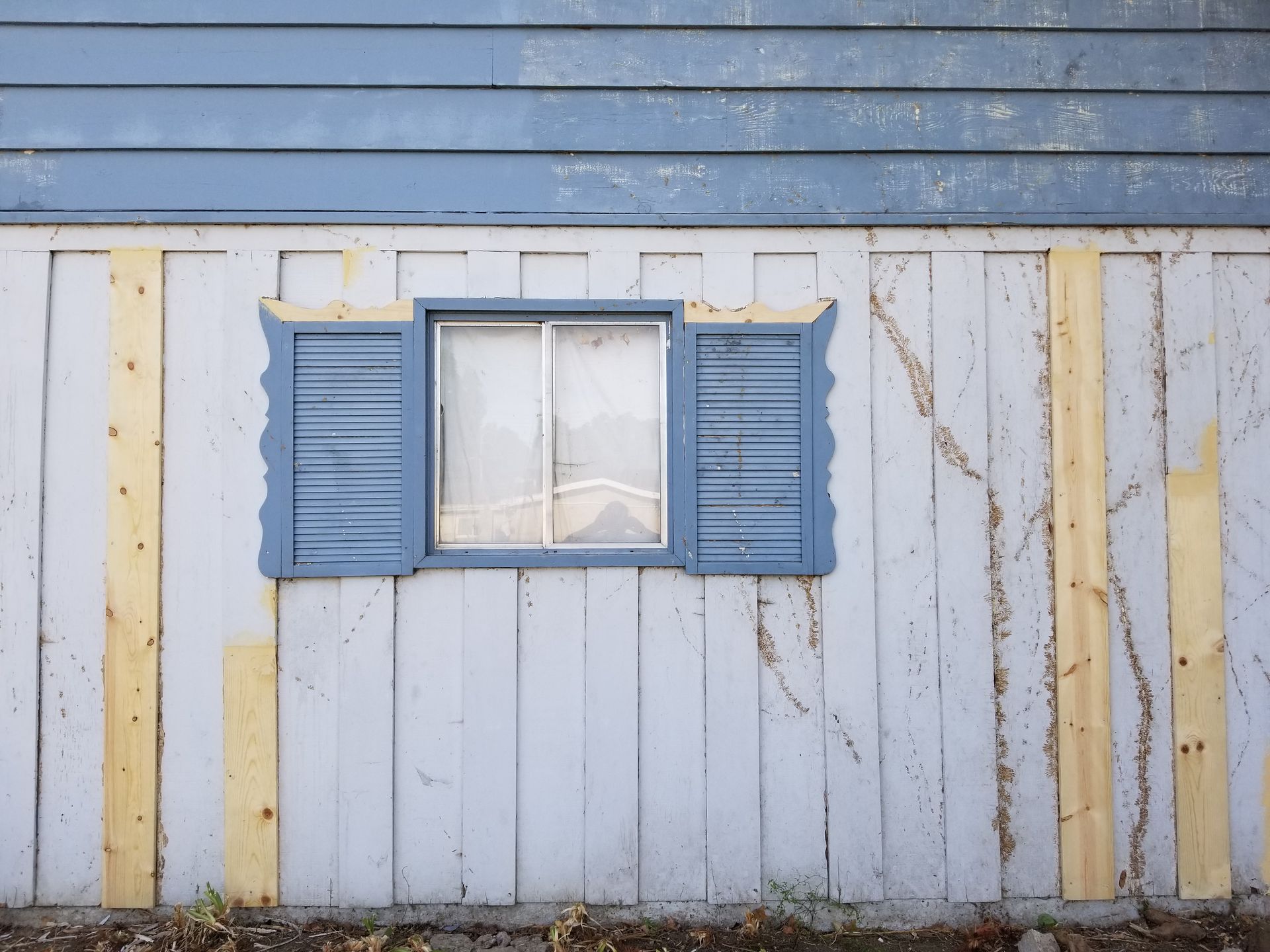 A blue and white house with a window with blue shutters on it.