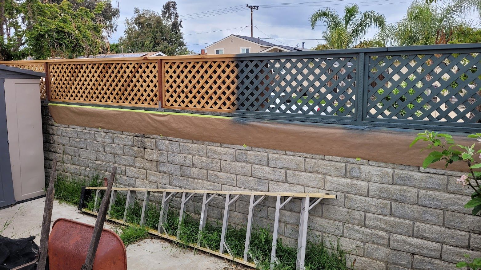 A brick wall with a wooden fence and a ladder in front of it.