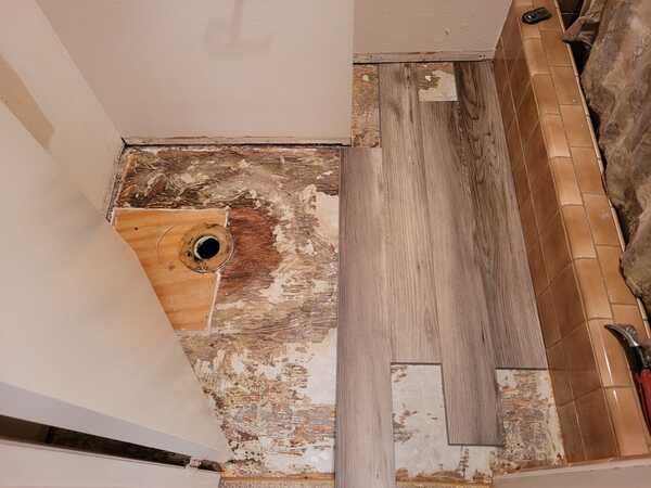 A bathroom with a wooden floor and a hole in the wall.