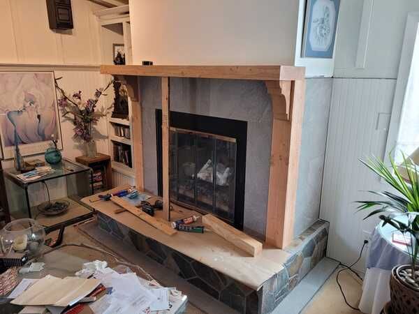 A living room with a fireplace and a wooden mantle being built.
