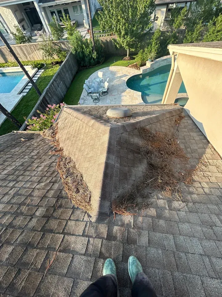 A person is standing on the roof of a house next to a pool.