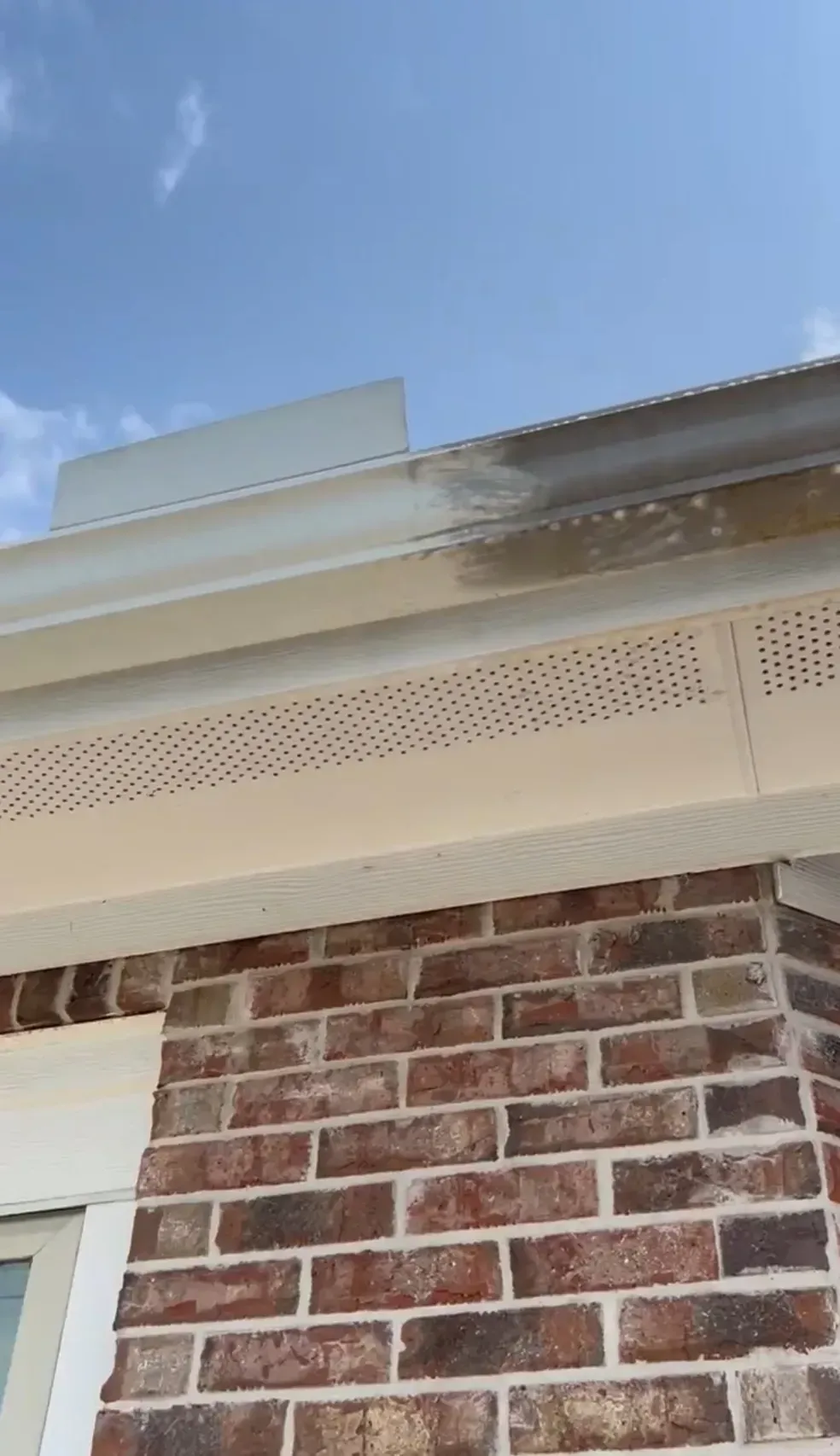 A brick building with a white gutter and a blue sky in the background.