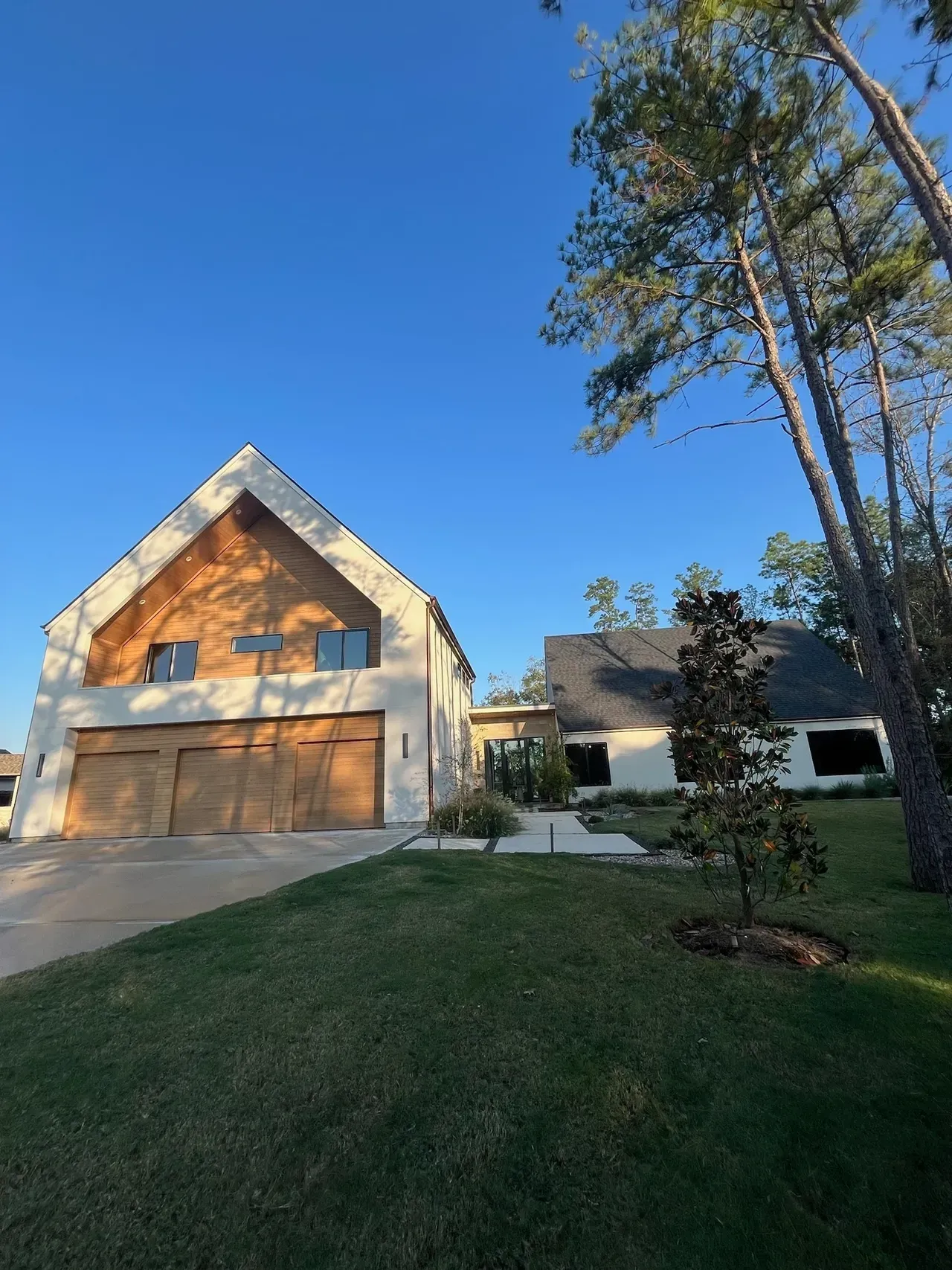 A large white house with a wooden garage door is sitting on top of a lush green lawn.