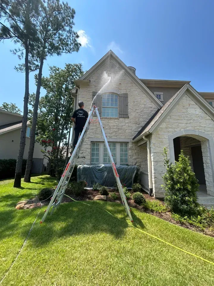 A man is standing on a ladder spraying a house with a hose.