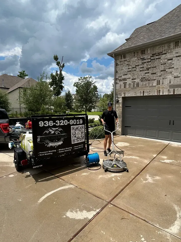 A man is cleaning a driveway in front of a house.