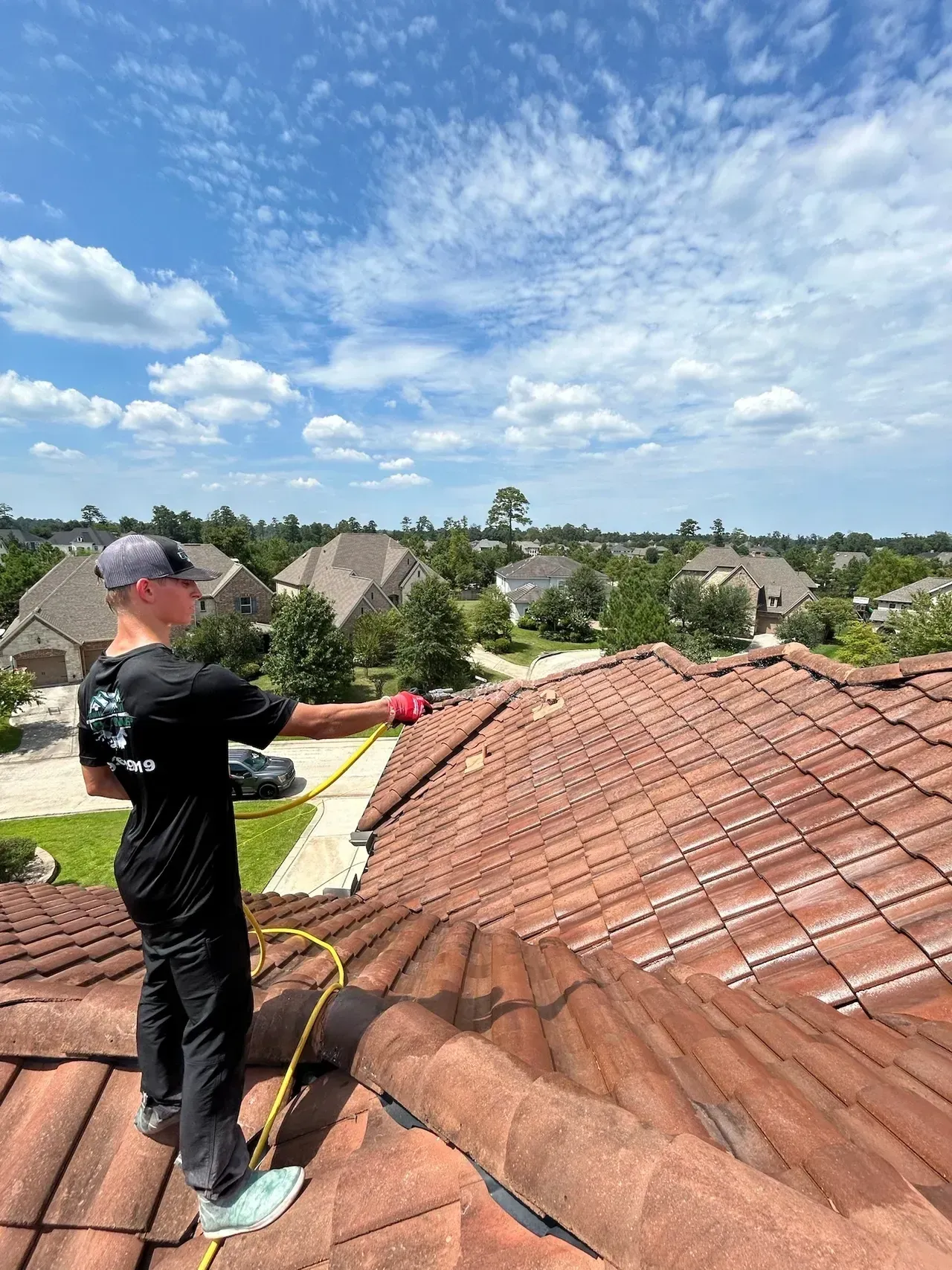 A man is standing on top of a tiled roof holding a hose.
