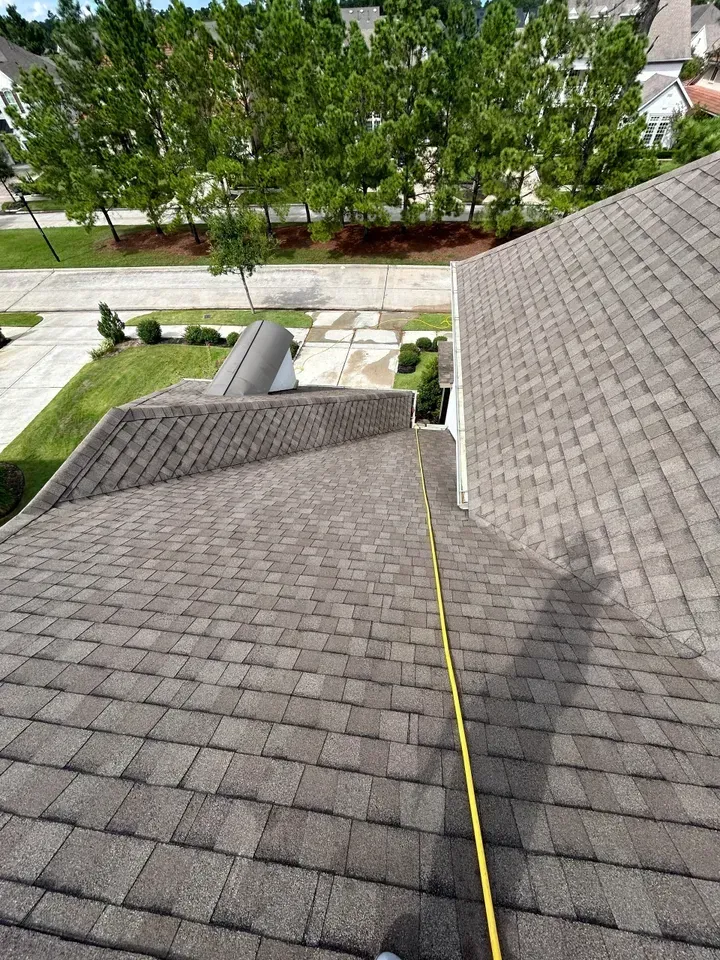 A person is measuring the roof of a house with a tape measure.