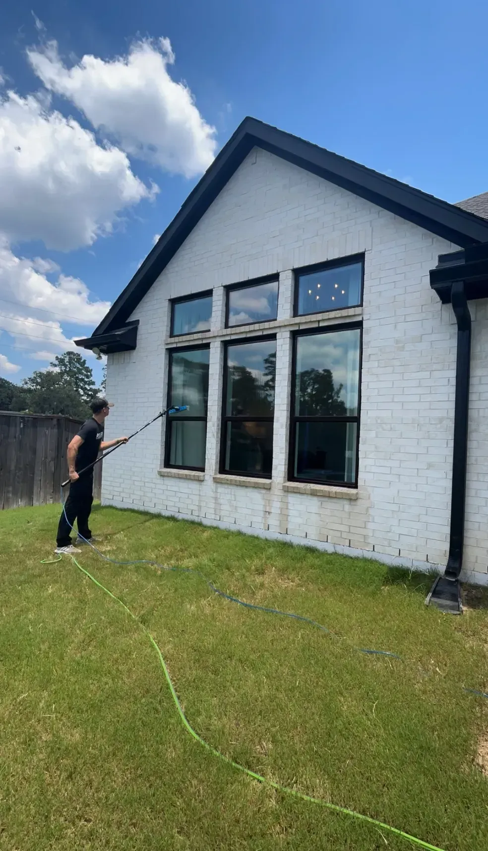 A man is spraying water on the side of a white house.