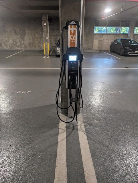 An EV charging station mounted on a concrete pillar in an indoor parking garage between two numbered parking spots.