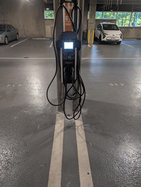 An electric vehicle charging station mounted on a concrete pillar in an indoor parking garage with two marked spaces.