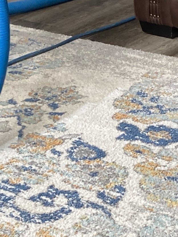 A close up of a rug in a living room with a blue hose.