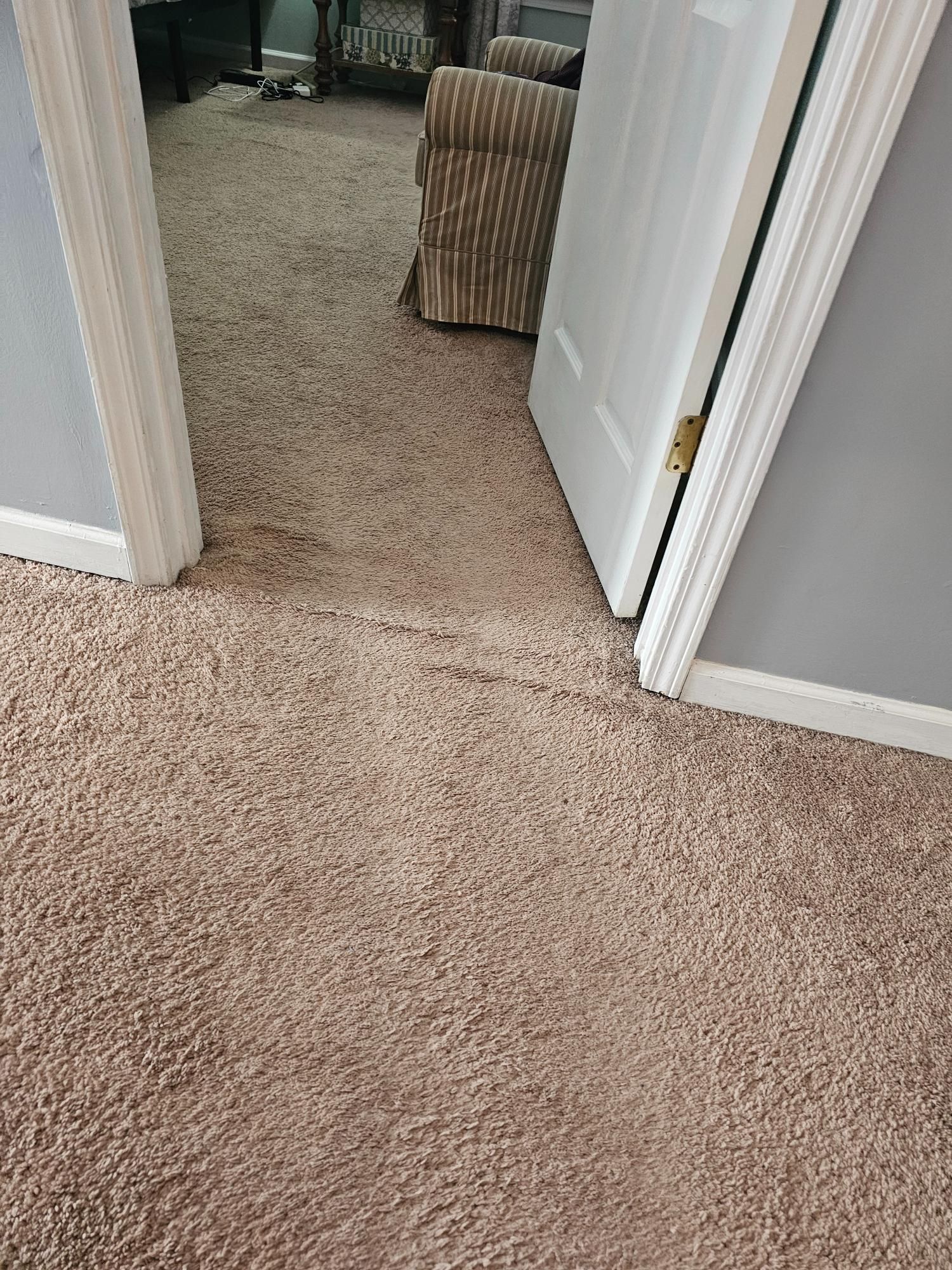 Beige carpeted hallway with slightly open white door, and a chair visible in the next room.