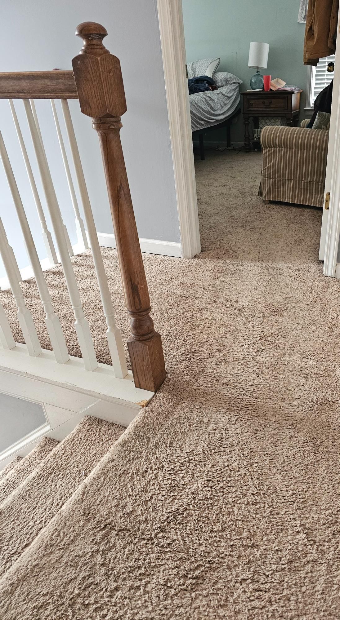 Staircase with brown carpet and a wooden banister leading up to a doorway with a bedroom visible.