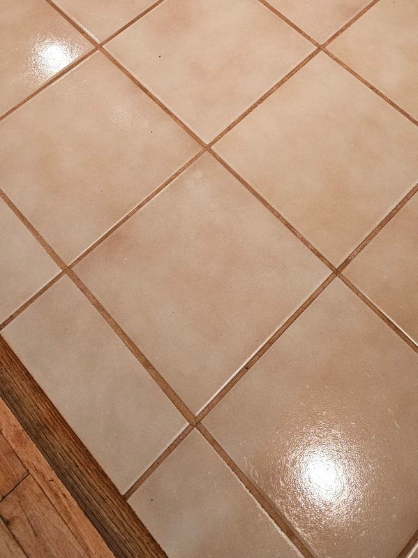 Beige diamond-patterned floor tiles with brown grout, next to a wooden floor.