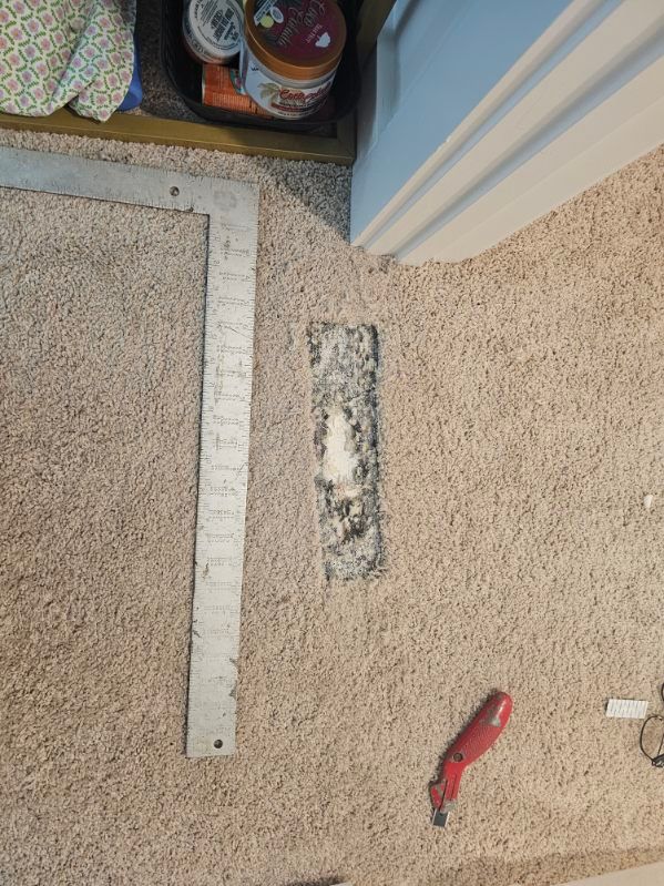 Beige carpet with a rectangular hole, a metal ruler, and a red cutting tool.