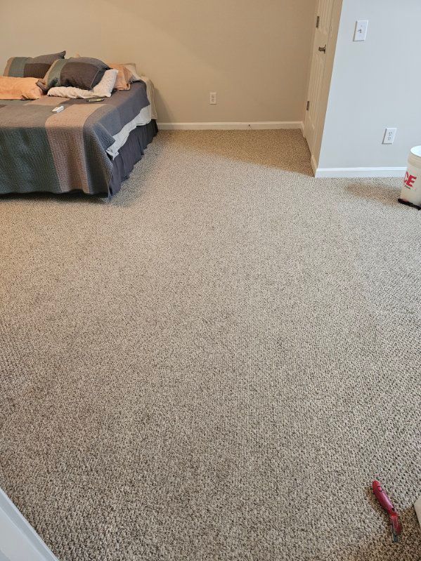 Bedroom with beige carpet, bed with gray blanket, and off-white walls.
