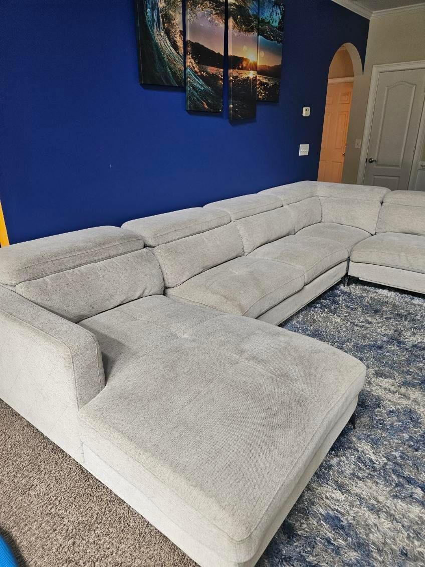 U-shaped gray sectional sofa on a blue rug in front of a dark blue wall; artwork above.
