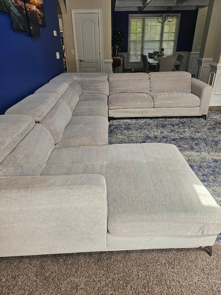 Beige sectional sofa on a blue rug, in front of a blue wall and window.