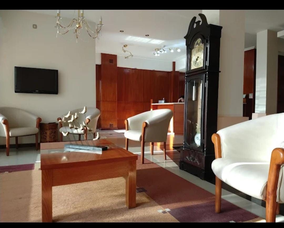 La mano de una persona abre la puerta de una habitación de hotel, revelando un dormitorio borroso con una cama y una ventana.