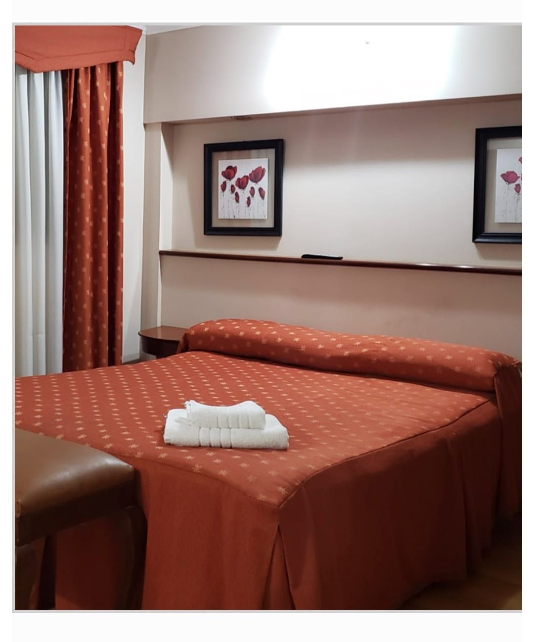 Habitación de hotel con cama, zona de estar y un gran espejo. Paredes beige, suelo de madera y colores neutros.