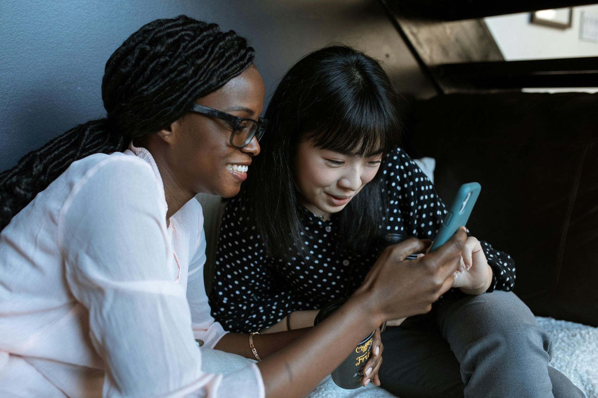 Two women are sitting on a couch looking at a cell phone