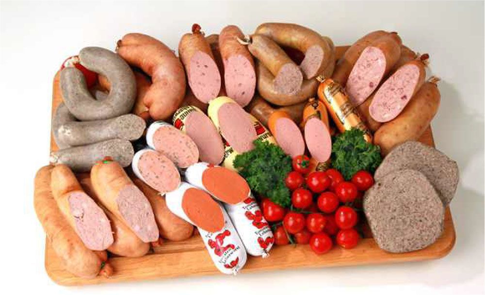 A variety of sausages and tomatoes on a wooden cutting board