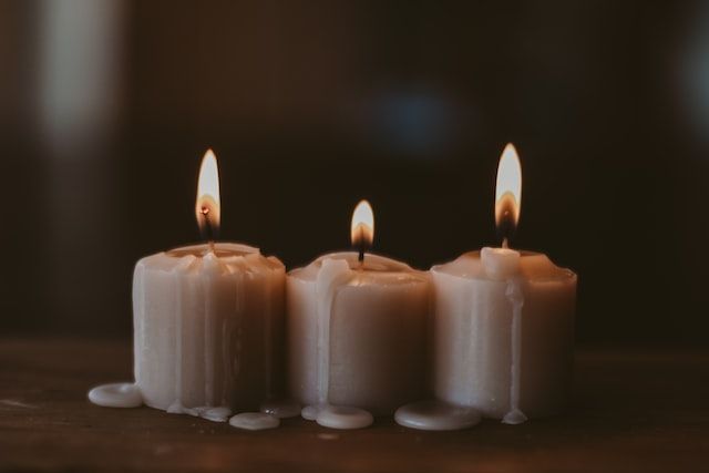 Three lit memorial candles with soft glowing flames and melted wax, symbolizing remembrance 