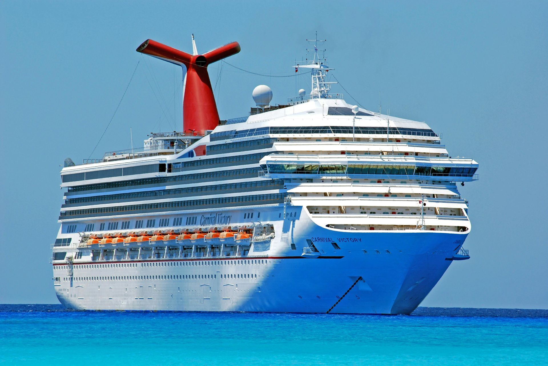 Cruise ship with red and white smokestack on blue water, under a clear sky.