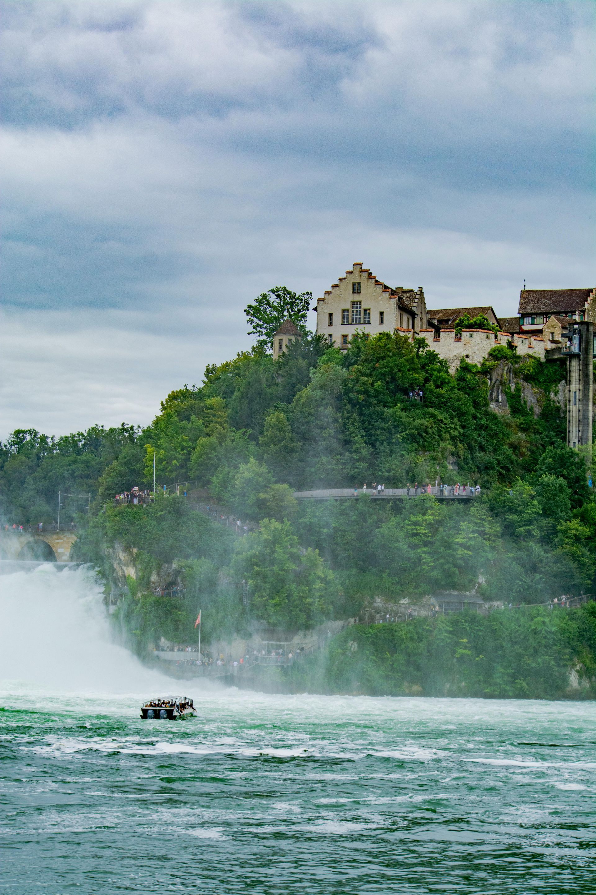 Waterfall with a castle on a tree-covered cliff, spray rising, and a boat on the water.