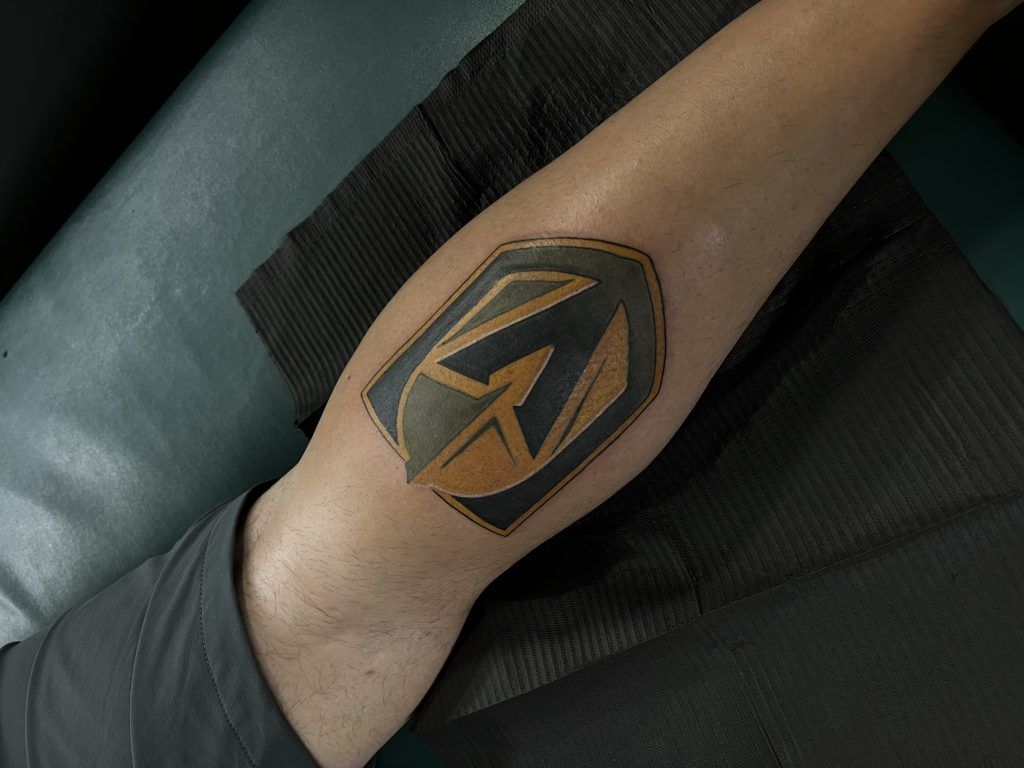 A person has a tattoo of a shield on their leg.