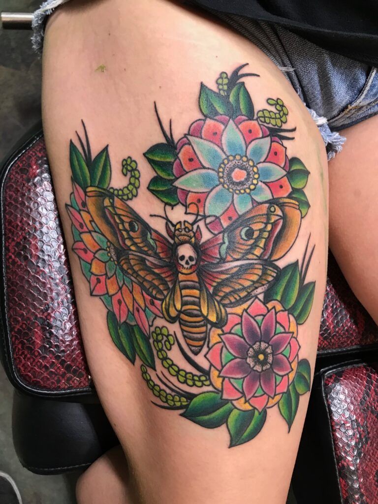 A woman has a tattoo of a moth and flowers on her thigh