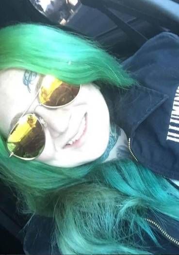 A woman with green hair and sunglasses is sitting in a car.