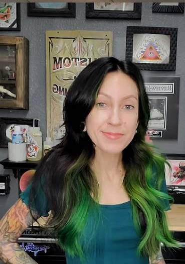 A woman with green hair is standing in front of a wall with pictures on it.