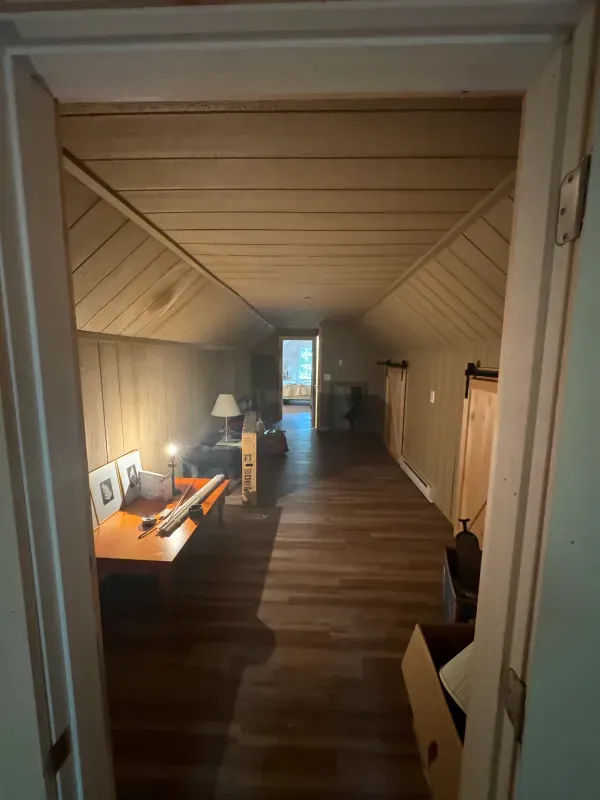 A hallway in an attic with a desk and a piano.