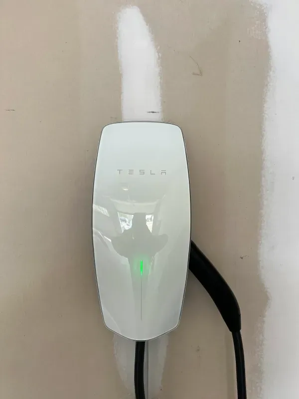 A white tesla charging station is plugged into a wall.