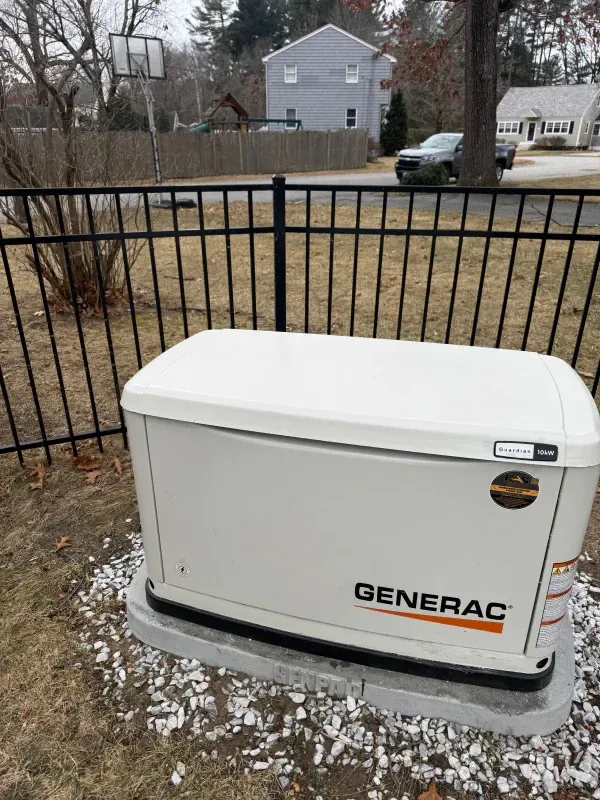 A generator is sitting in the grass next to a fence.