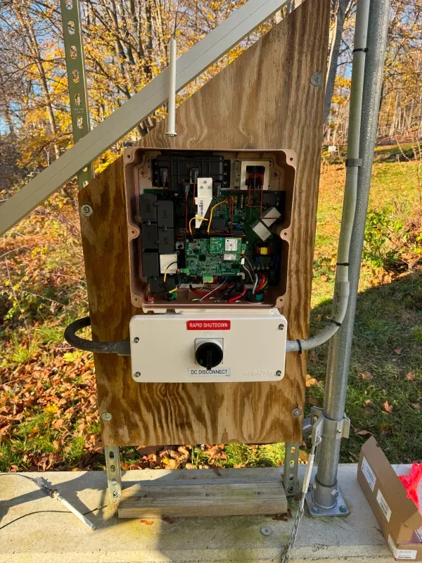 A white box is sitting on a wooden wall next to a metal pole.