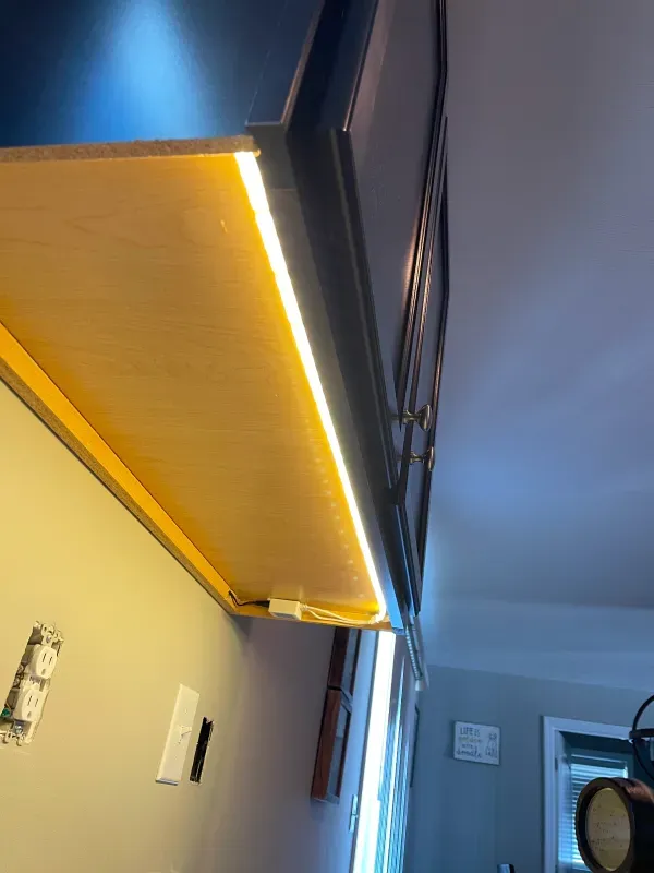 A person is standing under a cabinet with a light on it.