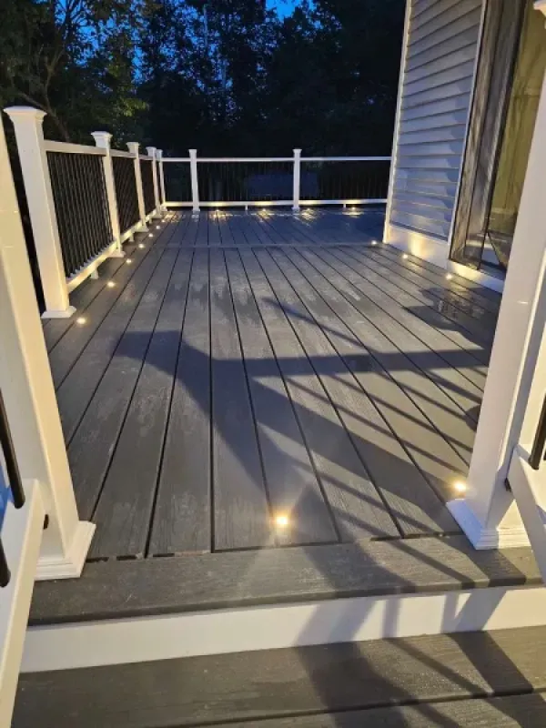 A deck with a white railing and lights on it at night.