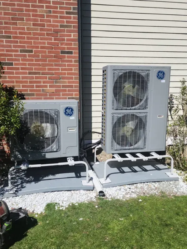 Two air conditioners are sitting next to each other in front of a brick building.