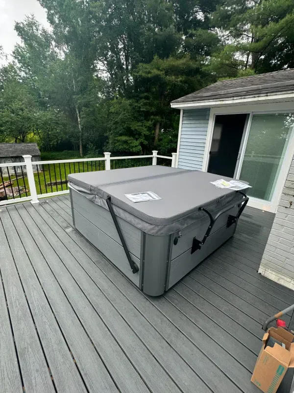 A hot tub is sitting on a deck next to a house.